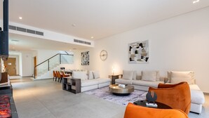 A modern living room with a sofa, coffee table, and orange chairs. There is a staircase leading to another level. - Exclusive 4BR Villa, Lush Garden & Private Pool Facing Panoramic Sea Views (Fujairah)