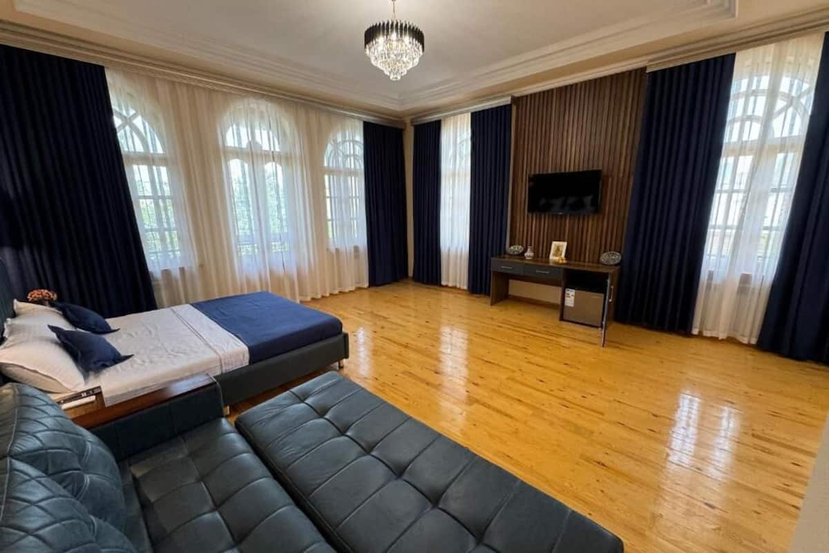 A spacious bedroom with a large bed, a seating area, a TV, and a wooden floor.