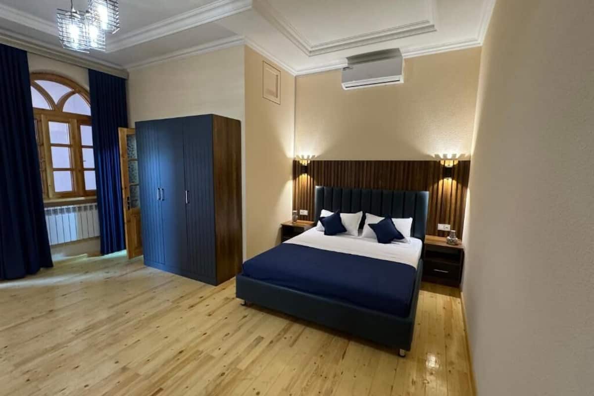 A bedroom with a large bed, wooden floor, a wardrobe, and a window with curtains.