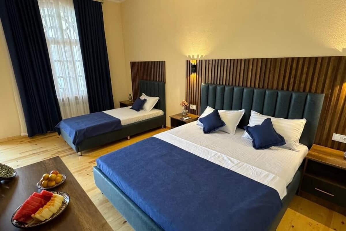 A hotel room with two beds, a wooden headboard, a nightstand, and a small table with fruit.