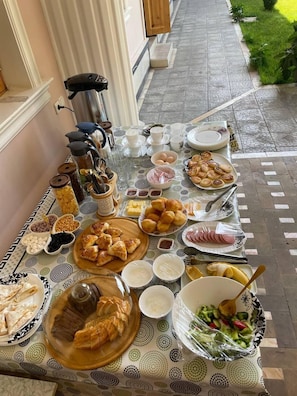 A breakfast buffet with various food items and utensils laid out on a patterned tablecloth. - Shakuri guest house (Samarkand)