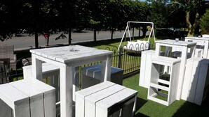 Outdoor seating areas with white tables and benches, surrounded by trees and a swing set. - 5 Star Holiday Home in Wangerland (Wangerland)