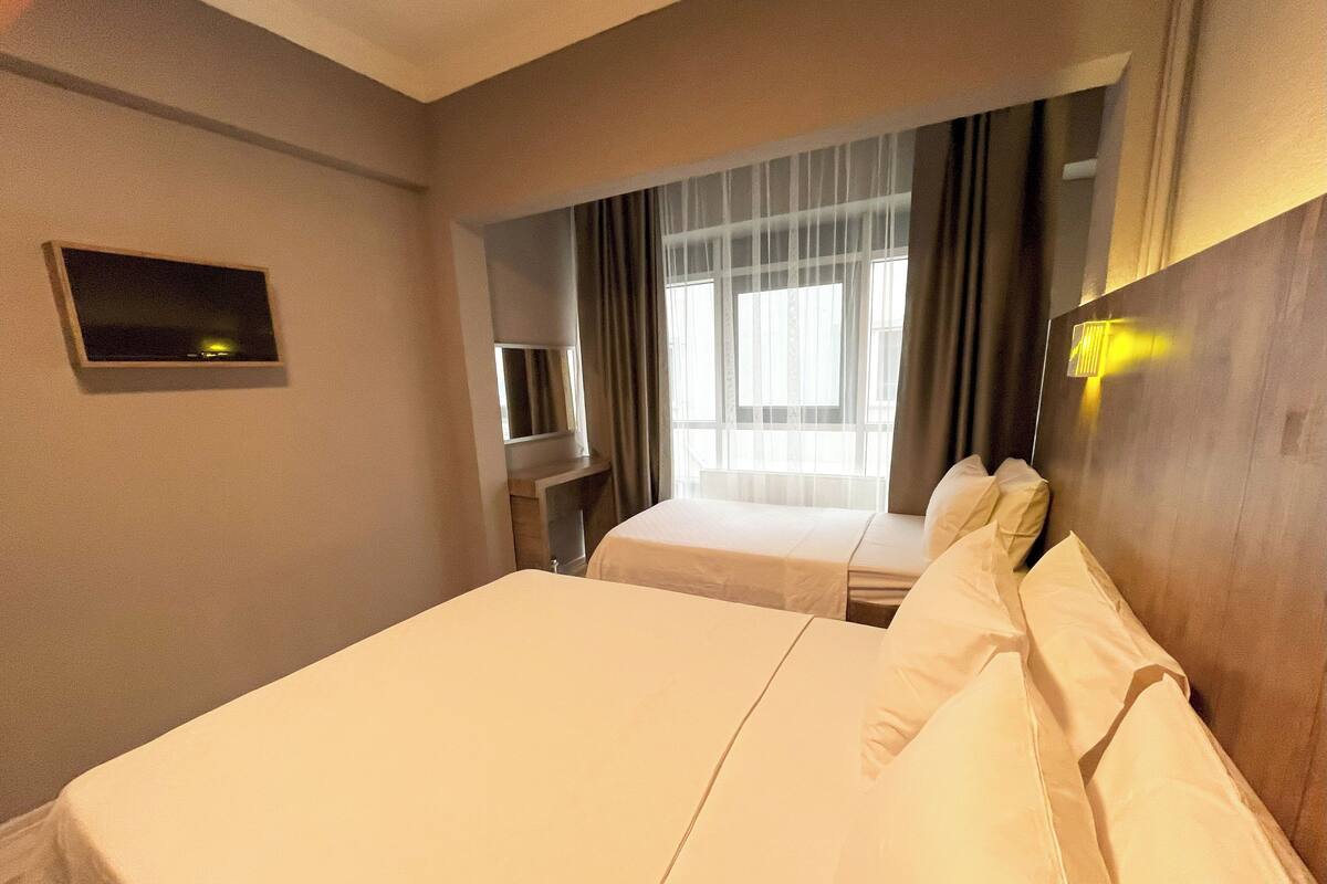 Una habitación de hotel con dos camas, televisión, ventana con cortinas y lámpara de noche.