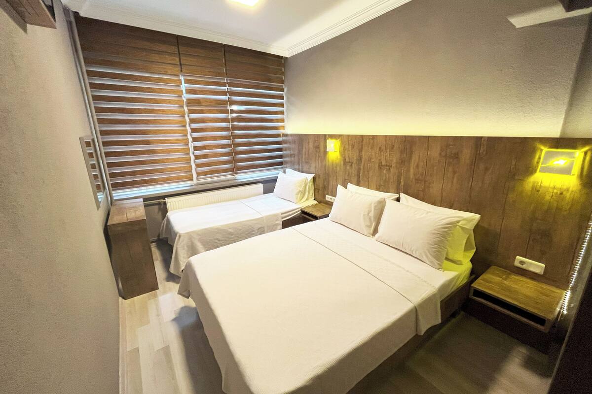Habitación de hotel con dos camas, cabecero de madera y ventana con persianas.