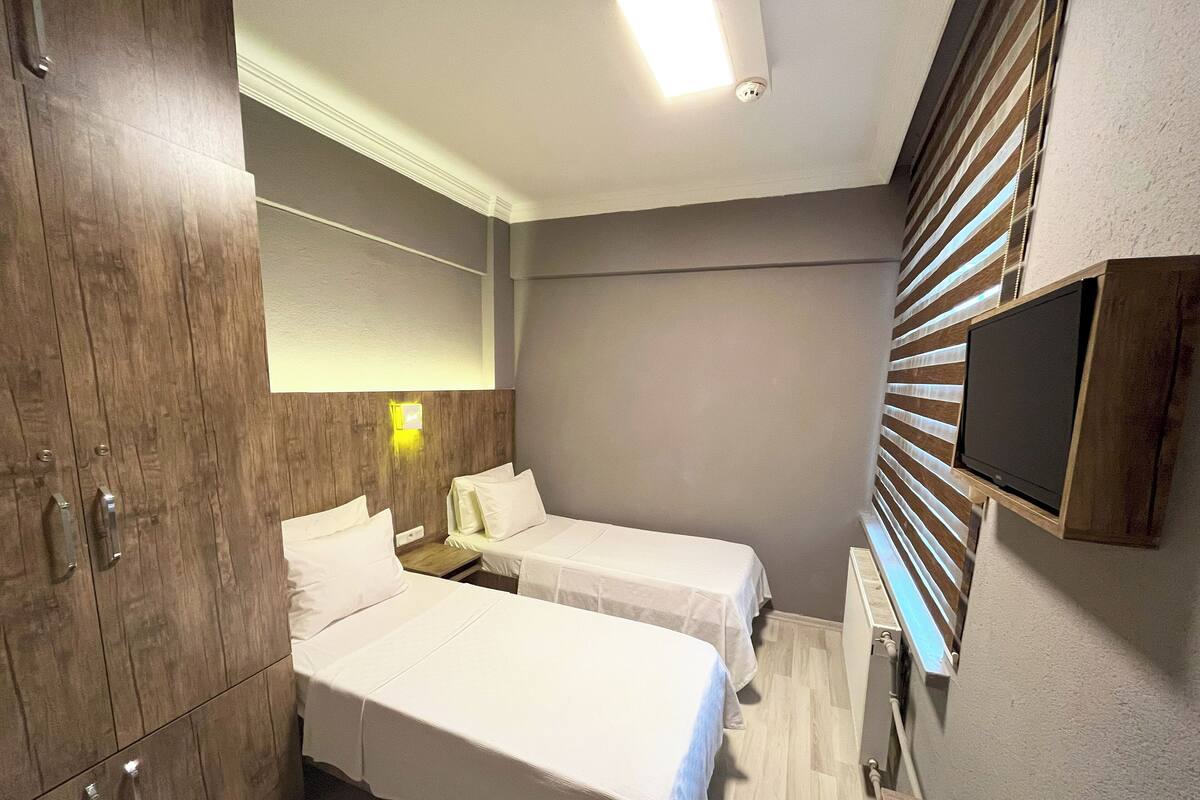 Habitación de hotel con dos camas, armario de madera, televisor de pantalla plana y lámpara de pared.