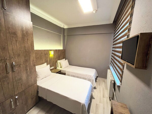 A hotel room with two beds, wooden wardrobe, a flat-screen TV, and a wall-mounted light.