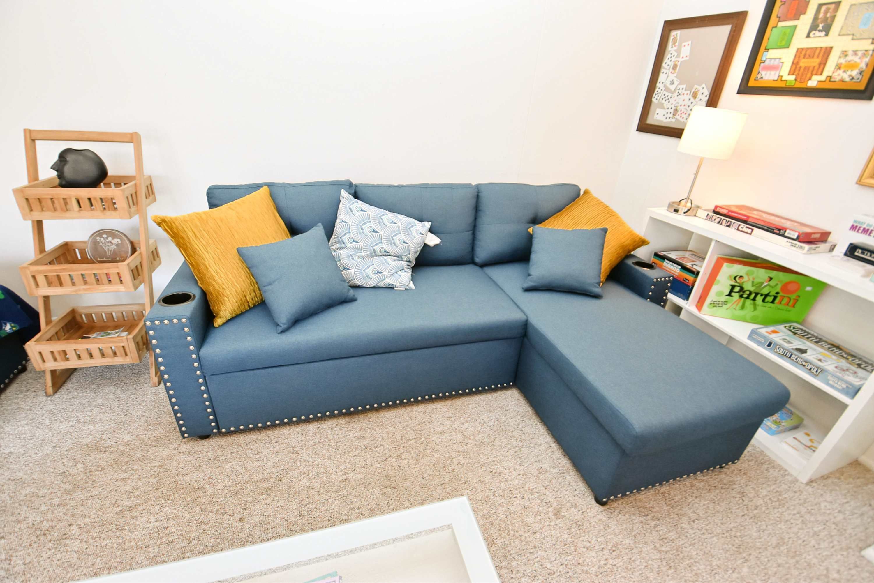 A modern living room with a blue sectional sofa, decorative pillows, a wooden side table, and a bookshelf.