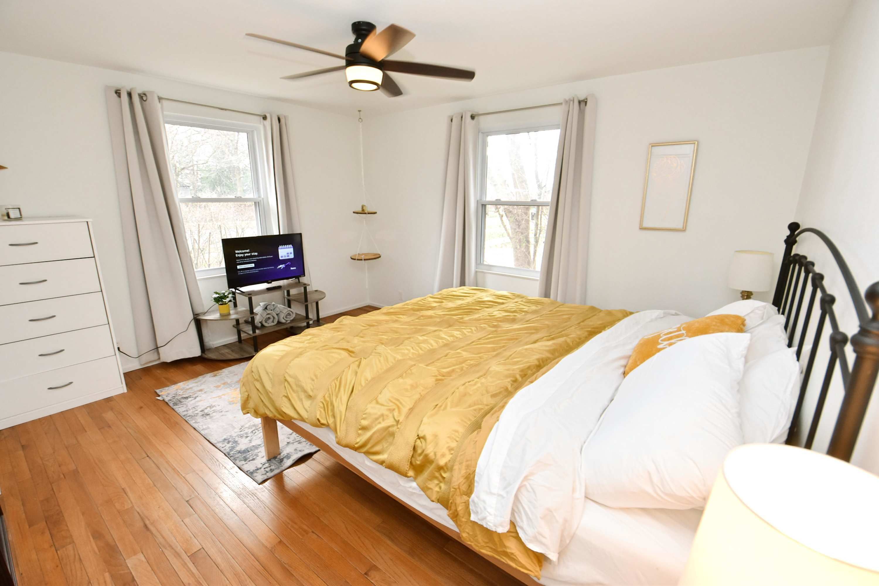 A bedroom with a bed, a desk with a computer, a ceiling fan, and a window.