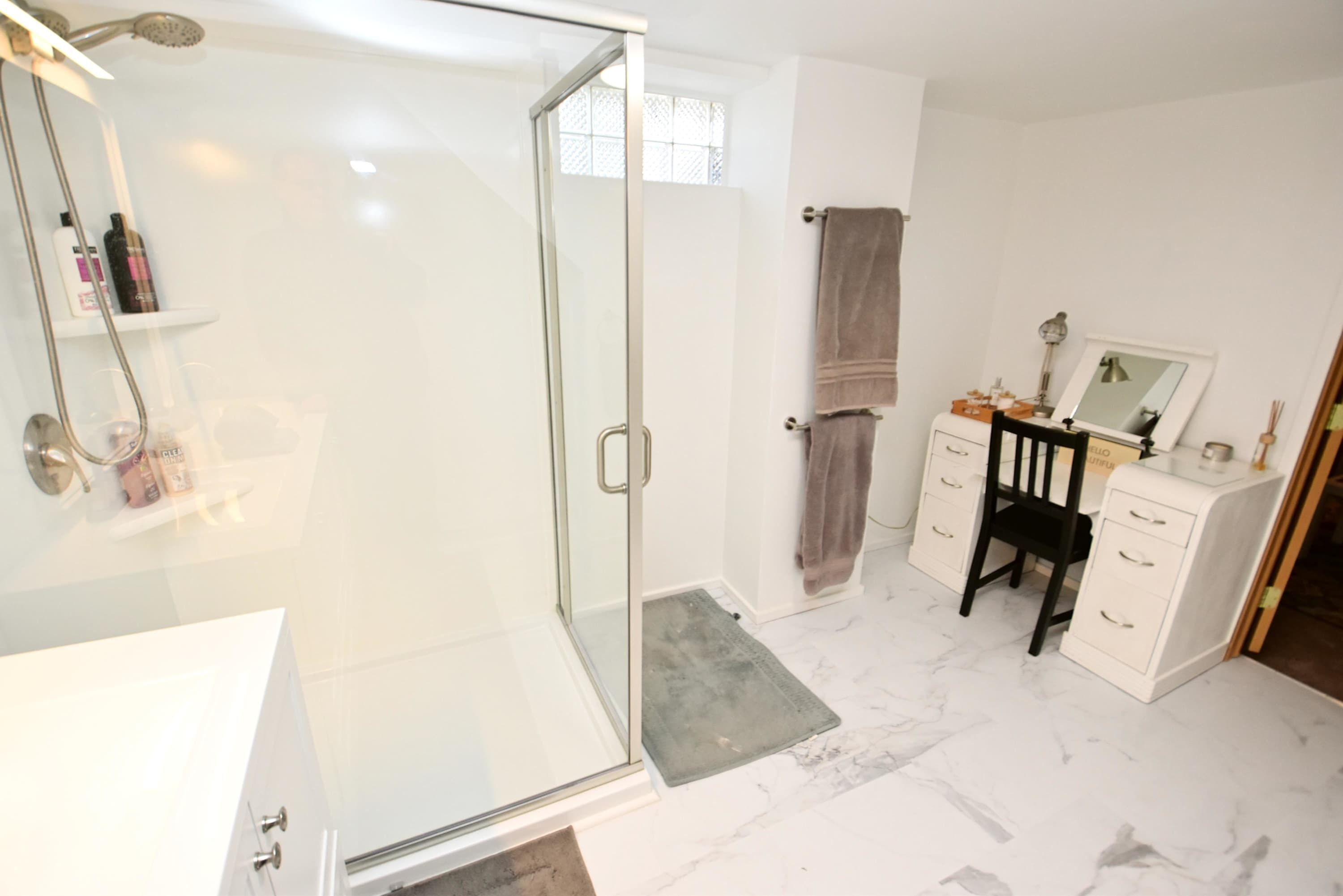 A bathroom with a glass shower enclosure, a vanity with a mirror, and a towel rack.