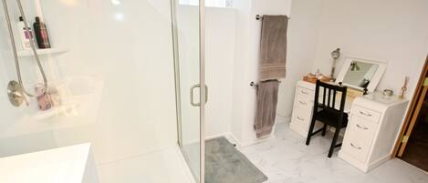 A bathroom with a glass shower enclosure, a vanity with a mirror, and a towel rack.
