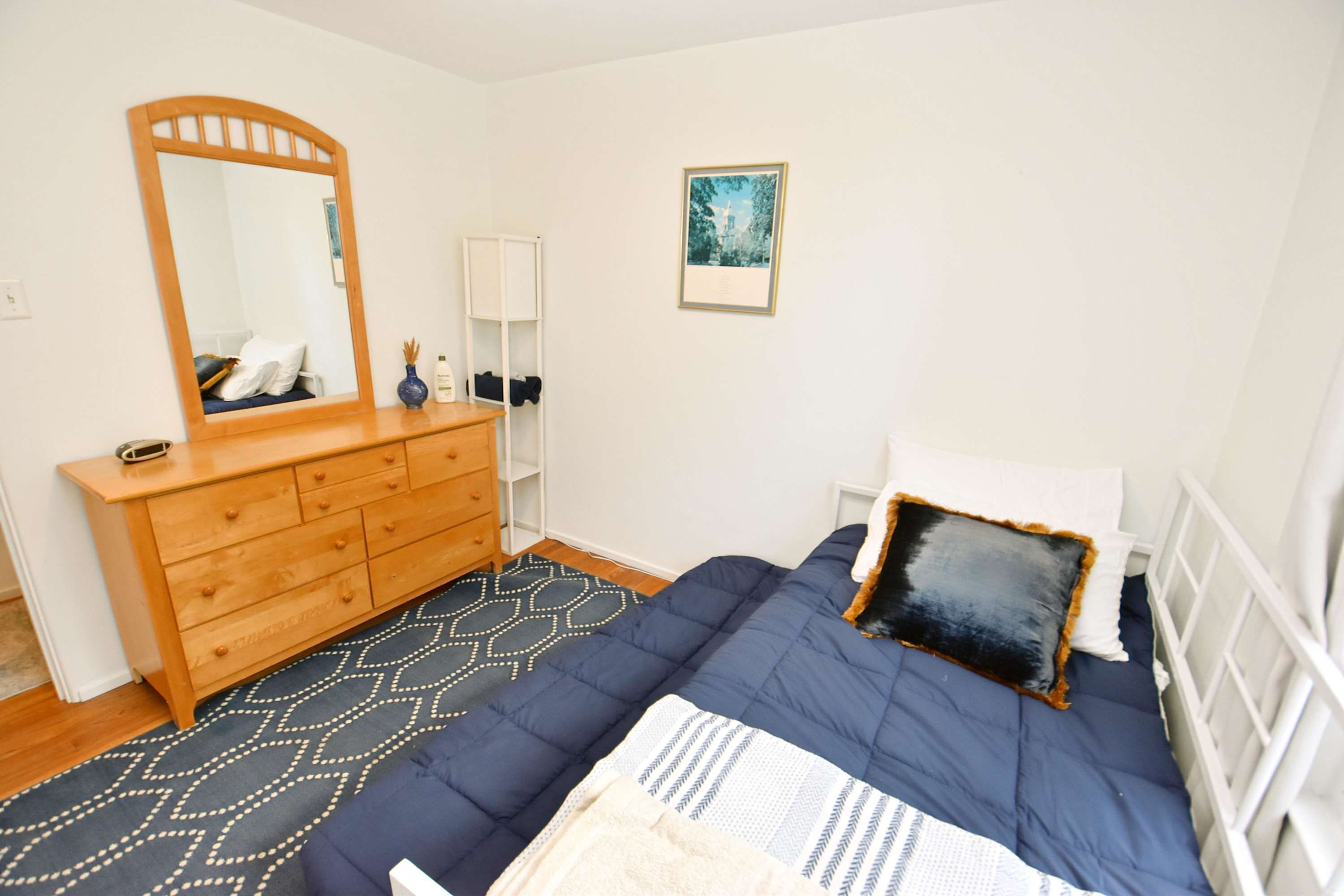 A bedroom with a bed, dresser, mirror, and a framed picture on the wall.