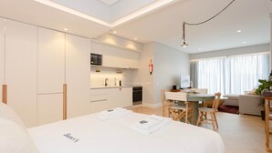 A modern hotel room with a bed, a dining area, and a kitchenette. - Liiiving in Porto - Luxury Design Apartment M (Porto)