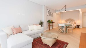 A modern living room with a white sofa, a glass coffee table, a dining area with a table and chairs, and a red patterned rug. - Liiiving in Porto - Luxury Design Apartment M (Porto)