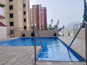 Piscina no terraço com deck de madeira, cercada por guarda-corpo metálico, com vista para um horizonte urbano com edifícios altos.