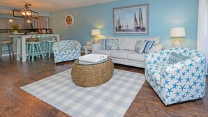 A living room with a checkered rug, a sofa, a chair, a coffee table, and a kitchen area with bar stools. - 2 BR Condo with Shared Pool! Sea Grove 202 (Surfside Beach)