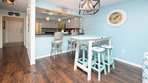 A kitchen with a bar area, wooden flooring, and a clock on the wall. - 2 BR Condo with Shared Pool! Sea Grove 202 (Surfside Beach)