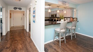 A kitchen with a light blue wall, wooden flooring, and bar stools. - 2 BR Condo with Shared Pool! Sea Grove 202 (Surfside Beach)