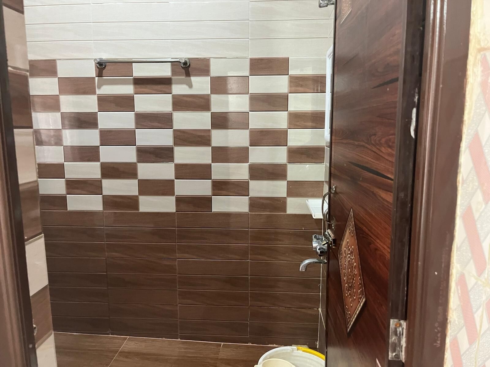 A bathroom with a checkered tile wall, a wooden door, and a visible toilet.
