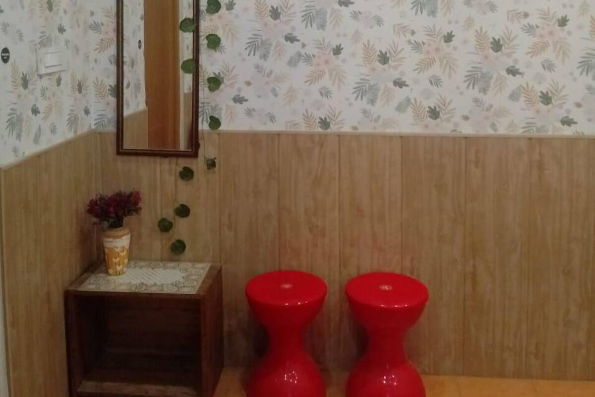 A bathroom with a floral wallpaper, a wooden vanity, a mirror, and two red toilets.