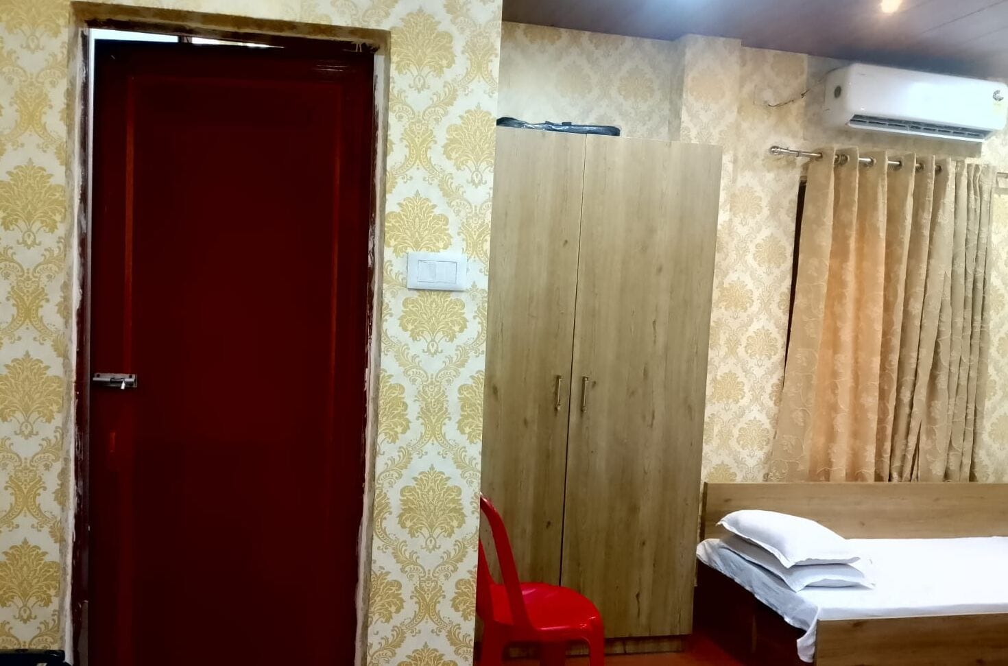 A room with a red door, wooden wardrobe, and a bed with white bedding.