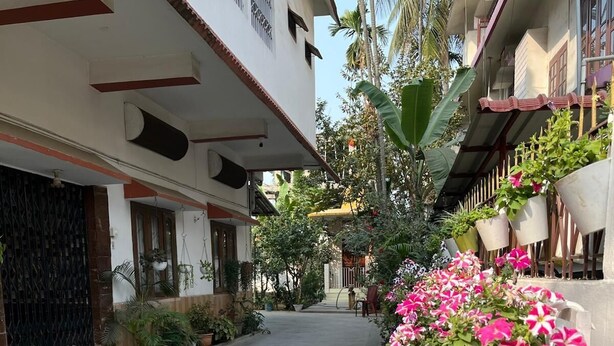 Une ruelle étroite dallée, agrémentée de plantes en pot et bordée, sur le côté droit, d’un immeuble doté d’un balcon.