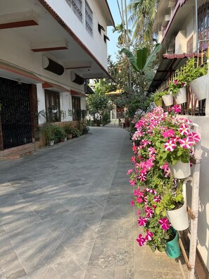 A narrow alleyway with tiled flooring, potted plants, and a building with a balcony on the right.