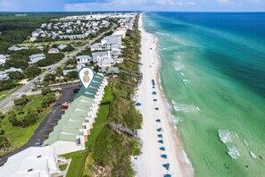 An aerial view of a coastal area with a row of beachside buildings, a clear beach, and the ocean.
