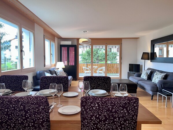 A modern living room with a dining area, large windows, and a balcony.