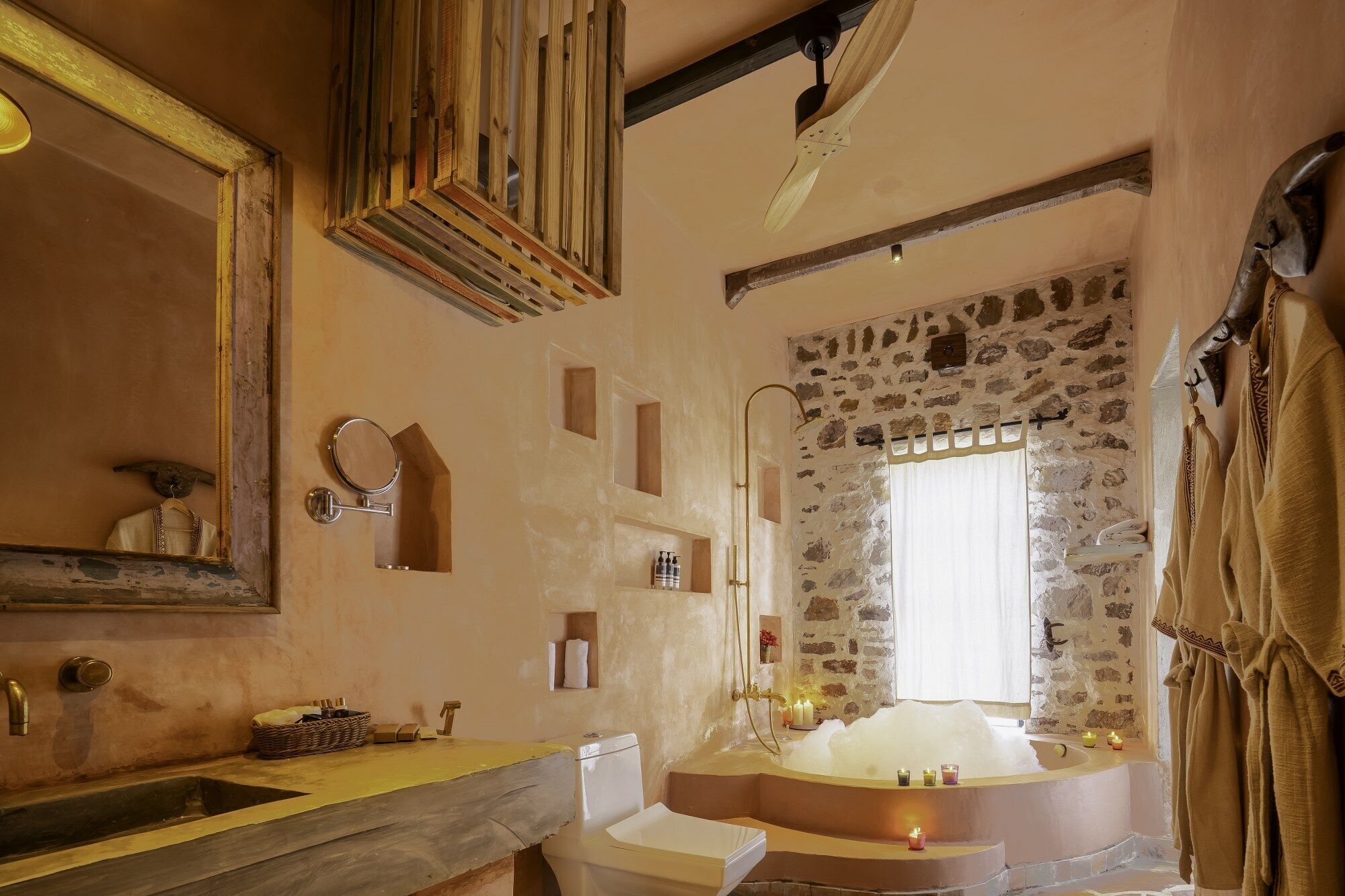 A rustic bathroom with a stone wall, a large bathtub, a wooden ceiling, and a mirror with a wooden frame.