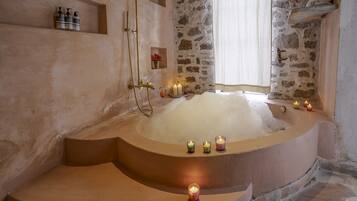 A spa bathroom with a large bathtub, stone walls, and candles.