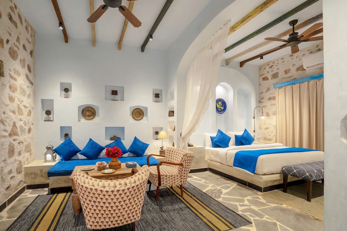 Ein Hotelzimmer mit Bett, Sofa und Essbereich, mit Steinwänden, Holzbalken und Deckenventilatoren.
