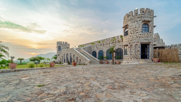 A stone building with a tower, arched windows, and a staircase leading to the entrance. - The Quila Udaipur by Aayor Luxury (Mavli)