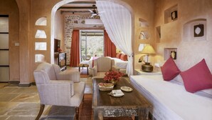 A cozy room with a bed, a sofa, a table with a vase of flowers, and a view of the outside. - The Quila Udaipur by Aayor Luxury (Mavli)