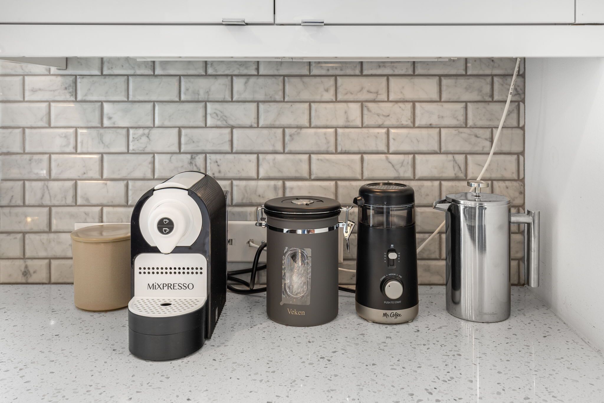 Een keuken met een koffiezetapparaat, waterkoker en koffiekan op het aanrecht.
