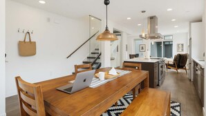 A modern kitchen with a wooden dining table, a laptop, and a hanging pendant light.
