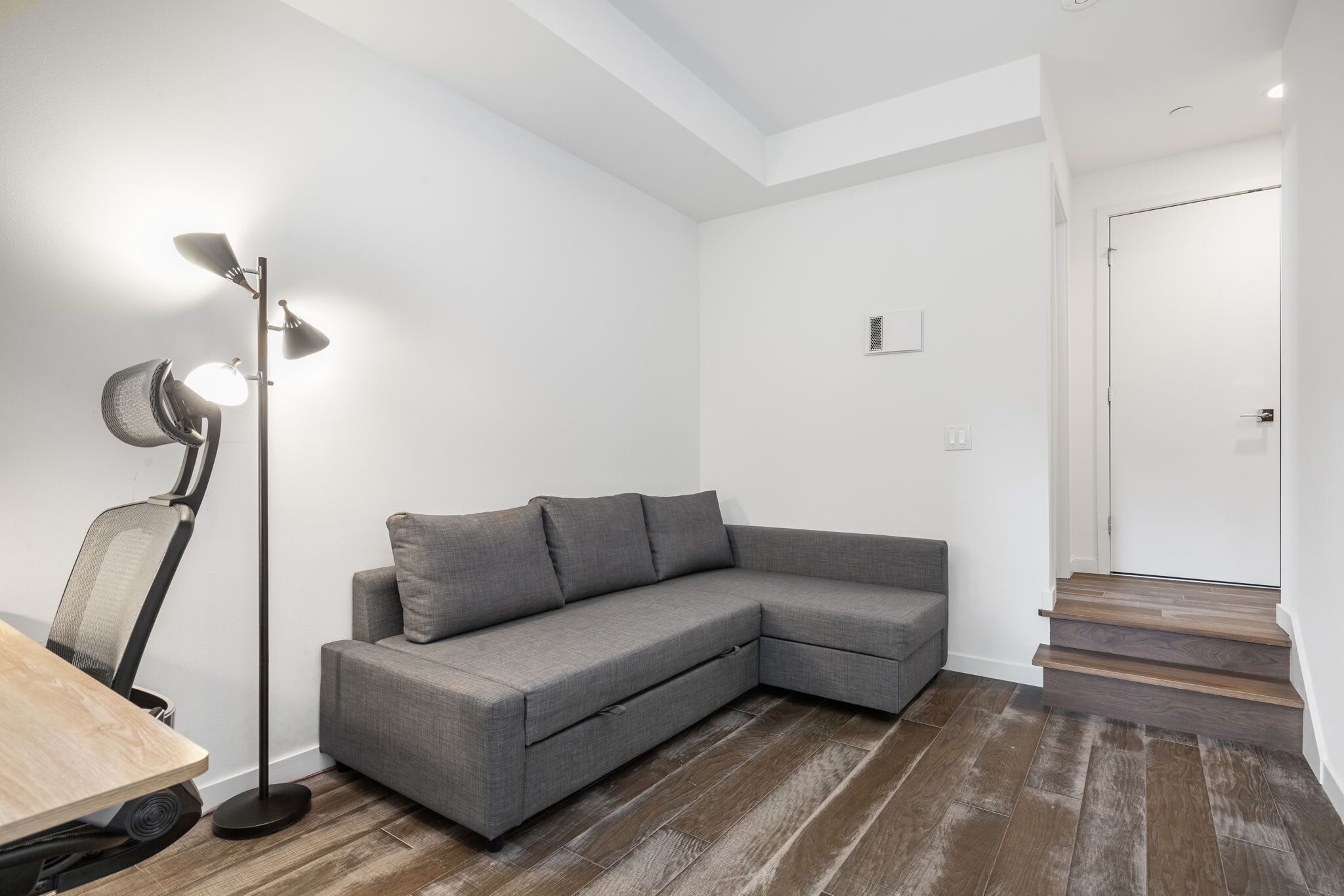 Una sala de estar moderna con un sofá modular gris, una lámpara de pie y una escalera que sube a un nivel superior.