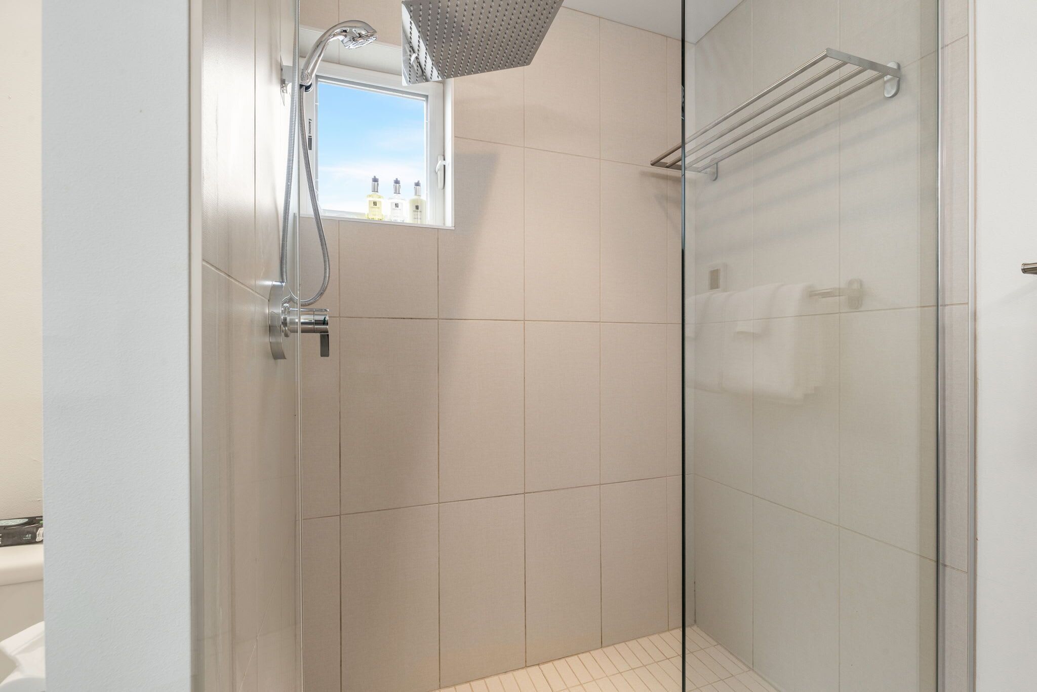 Un baño moderno con cabina de ducha de vidrio, un ventanal y un perchero para toallas.