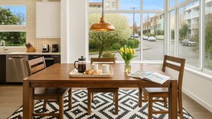 A modern kitchen with a dining area, large windows, and a view of the street.