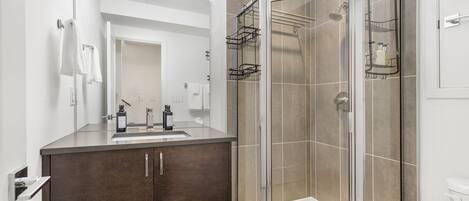A modern bathroom with a glass-enclosed shower, a dark wood vanity, and a large mirror.