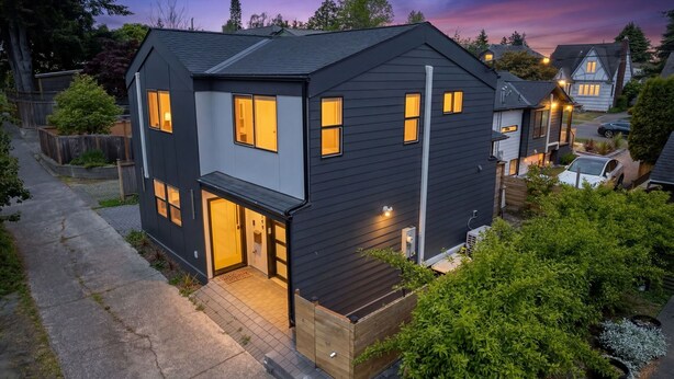 A modern two-story house with a dark exterior, multiple windows, and a well-lit entrance. - Sauna/Gym | Near Beach & Ballard | Dogs OK (Seattle)