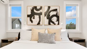 A bedroom with a large bed, two nightstands, a window with a view of a house, and two abstract paintings on the wall. - Sauna/Gym | Near Beach & Ballard | Dogs OK (Seattle)