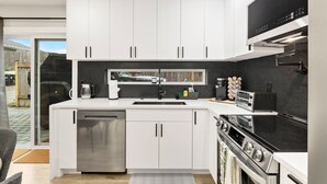 A modern kitchen with white cabinets, a built-in dishwasher, a stove, and a toaster. - Sauna/Gym | Near Beach & Ballard | Dogs OK (Seattle)