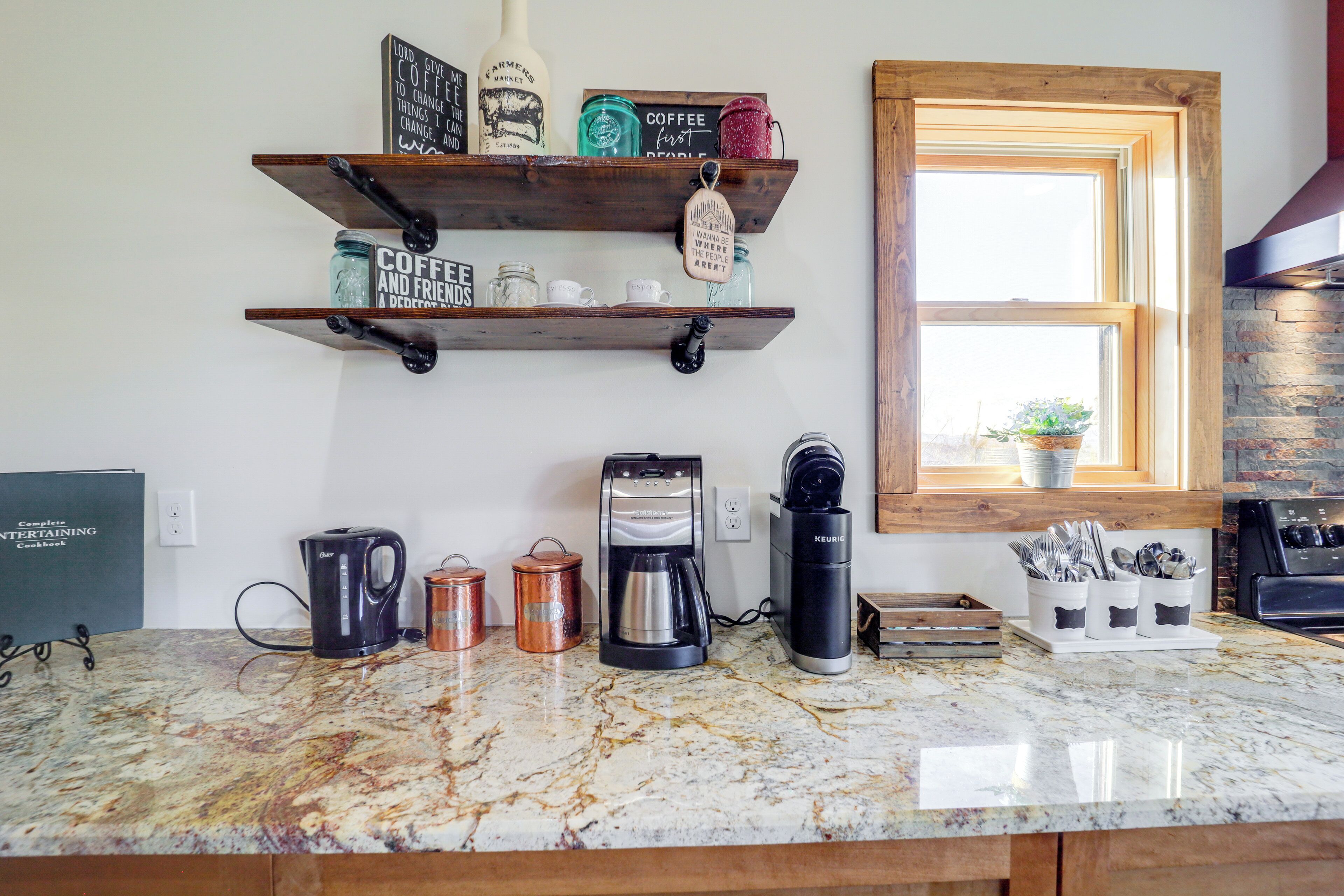 A kitchen with marble countertops, coffee makers, and shelves with coffee mugs and jars.