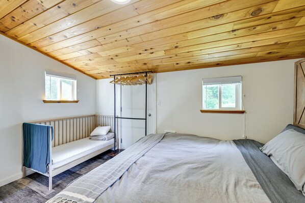 Une chambre avec un plafond en bois, un lit, un banc et deux fenêtres.
