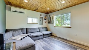 A modern living room with a sectional sofa, a glass coffee table, and a wooden ceiling.