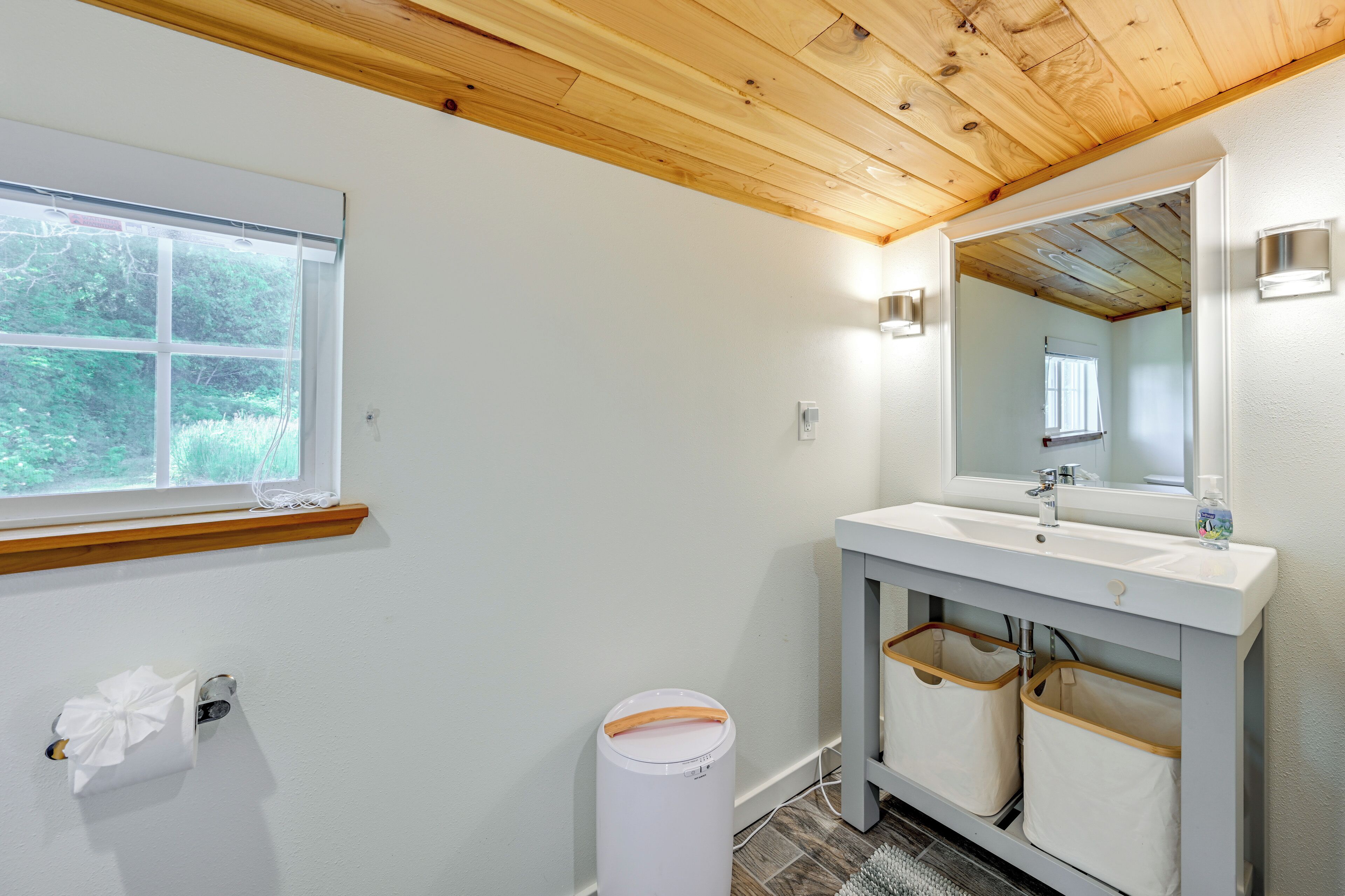 A bathroom with a wooden ceiling, a white sink with a mirror, and a window.