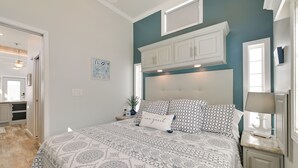 Een slaapkamer met een groot bed, een nachtkastje, een dressoir en een raam met gordijnen.