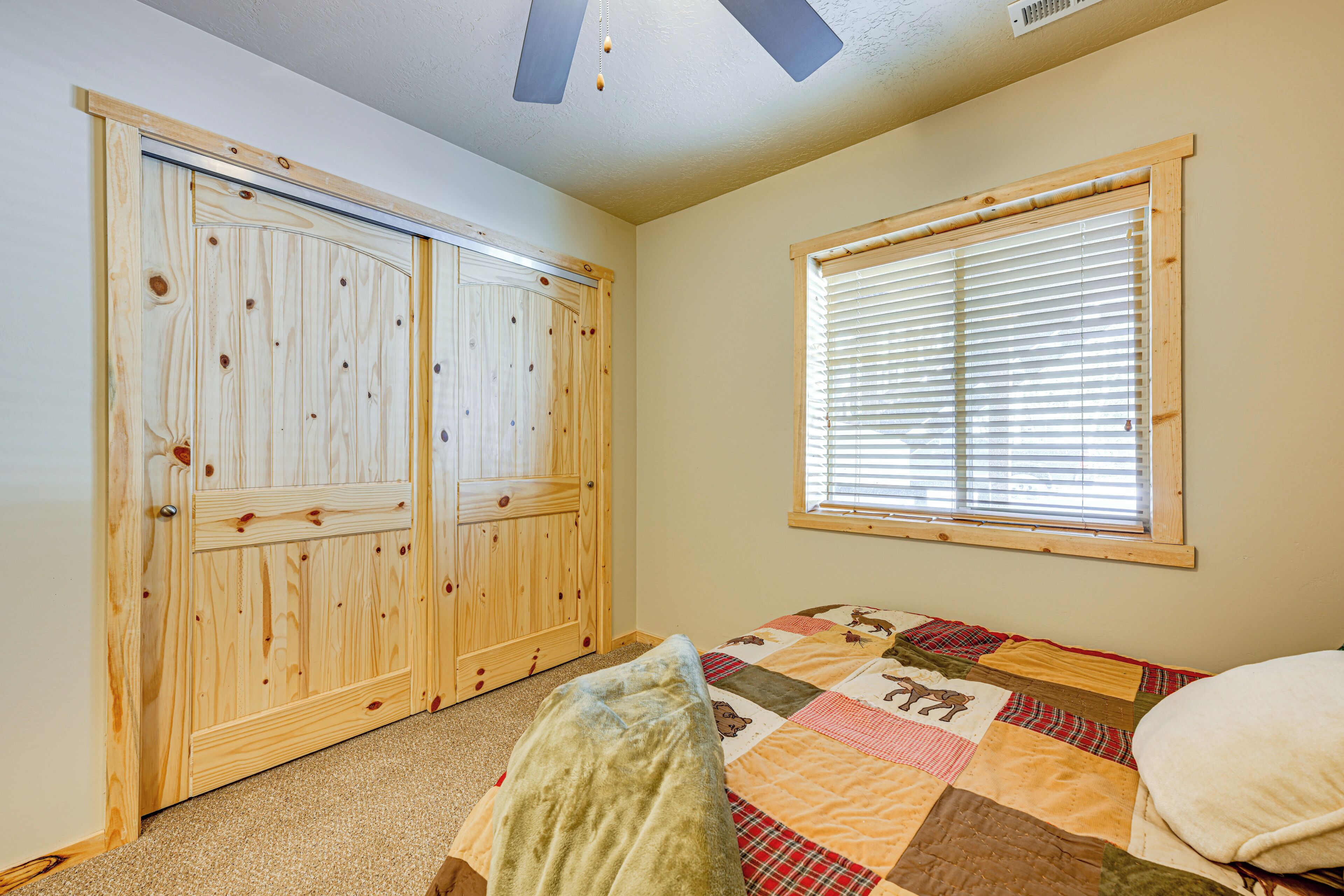 A bedroom with a wooden closet, a quilted bedspread, and a window with blinds.