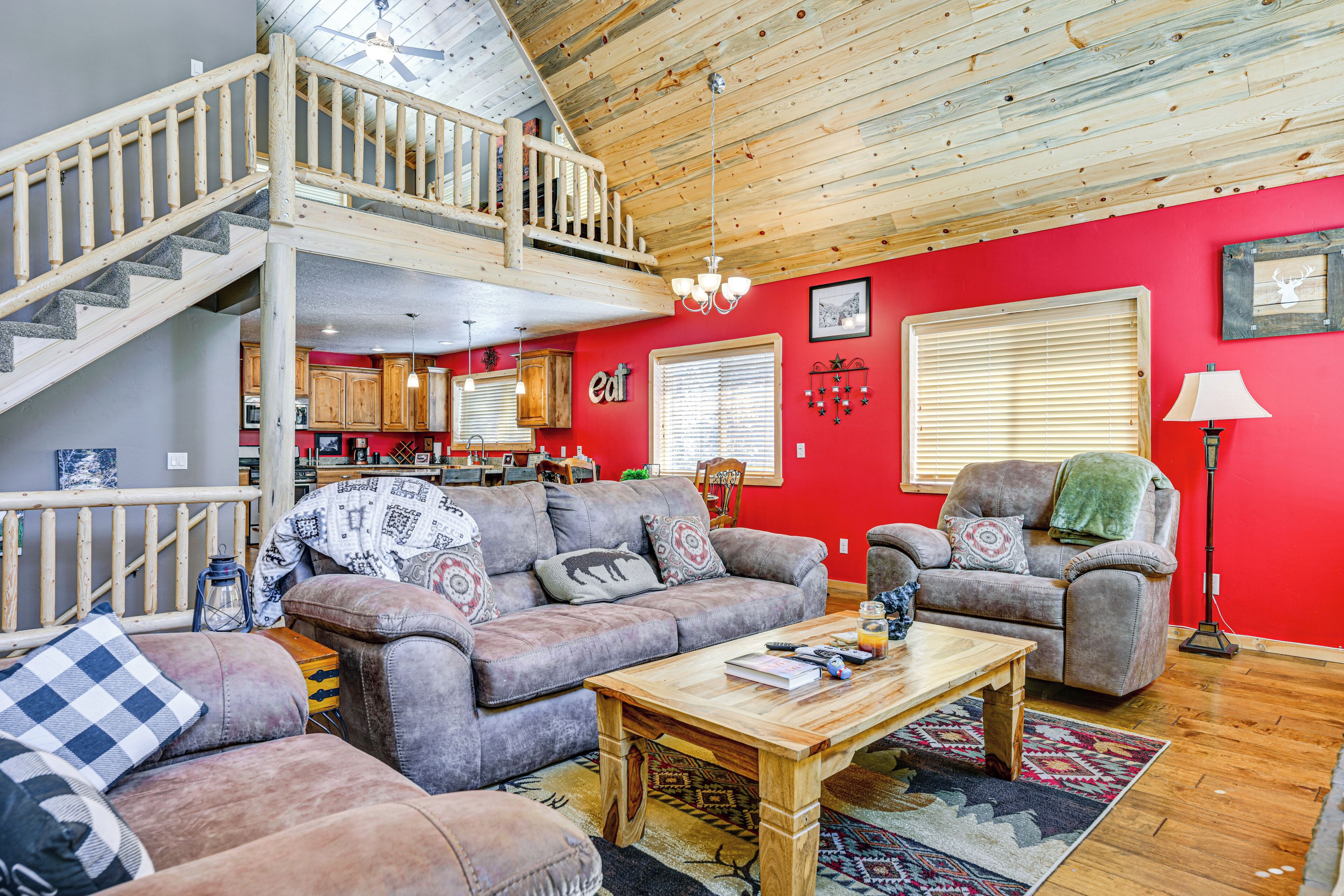 A spacious living area with a high ceiling, wooden staircase, and a red accent wall.