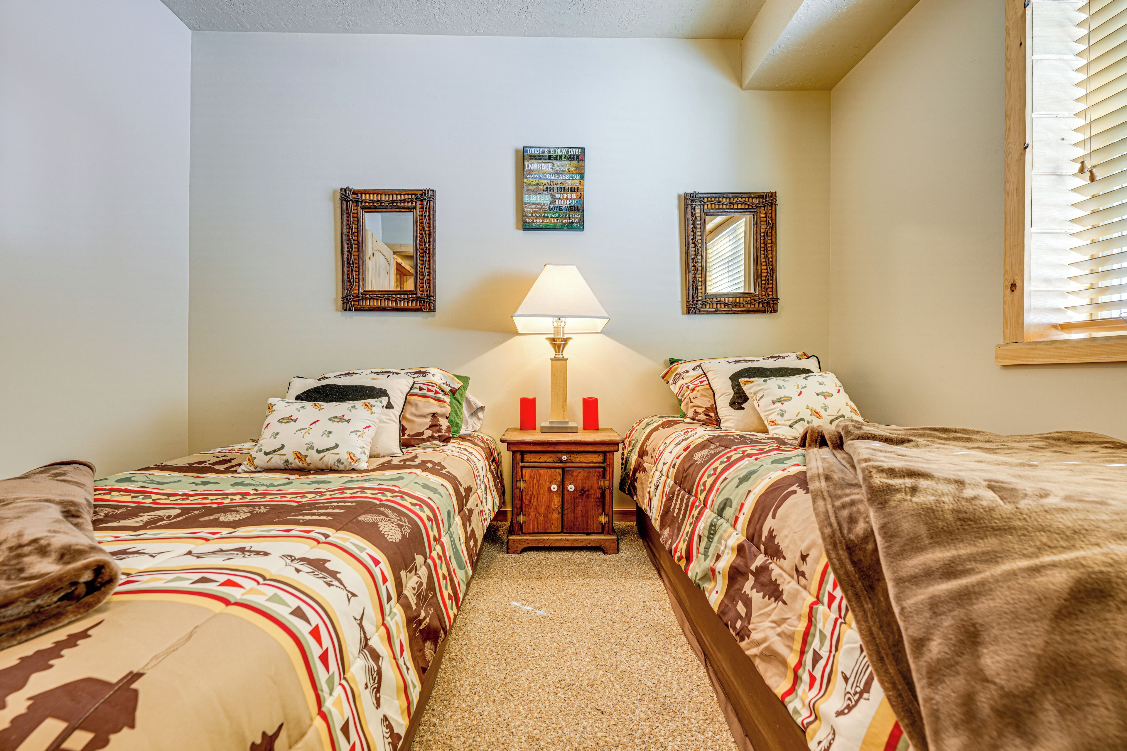 A bedroom with two beds, a nightstand, a lamp, and a wall-mounted mirror.